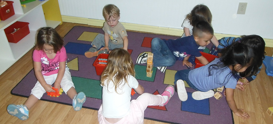 Young children playing with blocks on a classroom rug.