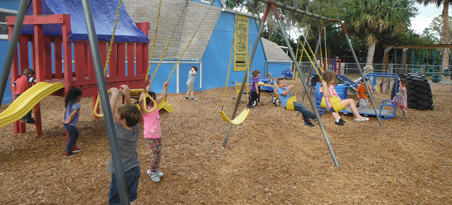 Children playing on swings and playground equipment outside.